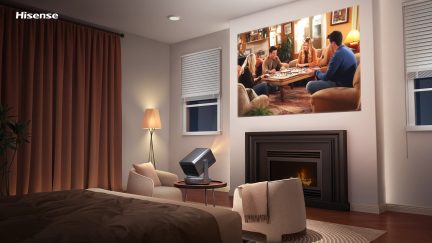 Vue intérieure chambre avec lit, rideaux marron, lampe sur pied, fauteuils, table basse, projecteur, cheminée, écran mural