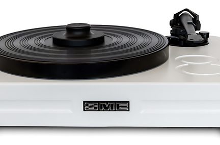 Pladespiller set forfra i close-up, sort rillet cirkulært pladetallerken med puck, sort tonearm til højre, rektangulær hvid satin metalbase med logo i relief