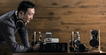 Un homme portant un casque audio se penche vers un amplificateur noir avec plusieurs casques audio sur des supports en bois.
