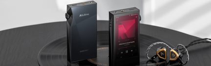 Două playere audio portabile negre cu ecran tactil și butoane laterale, însoțite de căști aurii pe un disc de vinil