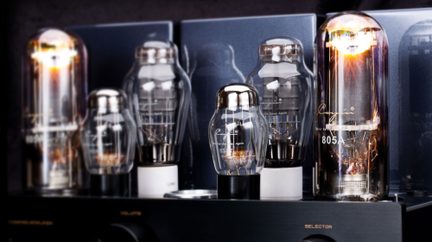 Close-up front view of several transparent glass vacuum tubes with silver-colored metal bases, mounted vertically on a black metal chassis, glowing orange filaments and visible white markings
