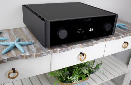 Amplificateur noir rectangulaire avec boutons circulaires, écran affichant "45", posé sur meuble en bois avec étoiles de mer