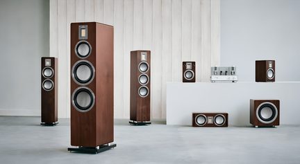 Ensemble de haut-parleurs hi-fi en bois brun à cônes gris métallisé et tweeters rectangulaires, vue d’ensemble frontale légèrement latérale dans une pièce minimaliste