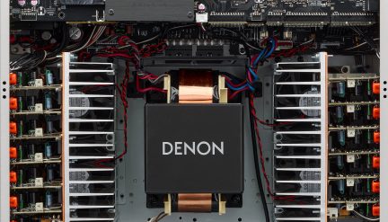 Vue interne amplificateur Denon, transformateur central noir, câbles rouges et bleus, dissipateurs thermiques métalliques