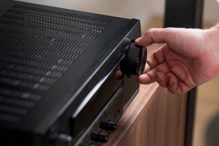 Main tenant un bouton rotatif sur un appareil électronique noir avec grille de ventilation, vue rapprochée de côté