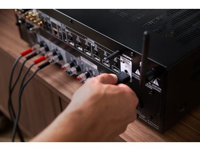 Ampli hi-fi stéréo Denon DRA-900H noir, vue rapprochée de la face arrière, connectique audio et antenne, main sur un connecteur