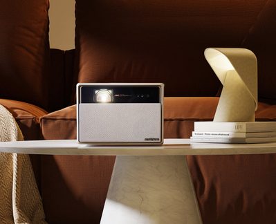 Projecteur 4K sur étagère blanche entre lampe dorée et livres, dans pièce aux murs et rideaux marron
