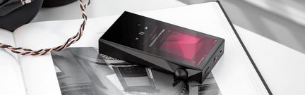Player audio portabil negru cu ecran tactil afișând o interfață muzicală, buton rotativ și conectivitate pe lateral.