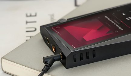 Baladeur audio noir avec écran affichant un graphique rouge, connecté à un câble noir, posé sur un livre ouvert