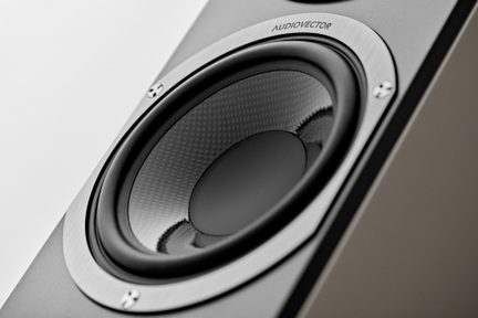 Gros plan en vue de trois quarts sur un haut-parleur hi-fi gris, cône noir à texture tressée et entourage en aluminium brossé fixé par quatre vis