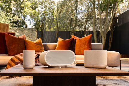 Casse wireless Denon beige su tavolino basso in legno davanti a un divano da esterno con cuscini arancioni