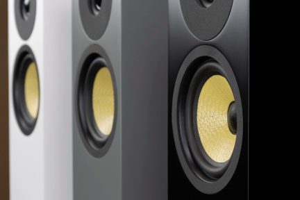 Close-up view of three vertical speakers with textured yellow cones and black edges, featuring black, gray, and white finishes.