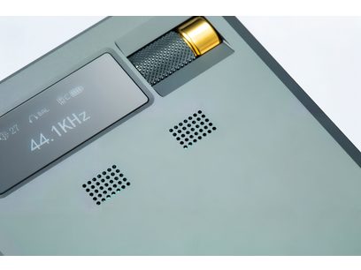 Portabel ljudomvandlare Cayin RU9 i matt grön aluminium, närbild i trekvartsvy som visar monokrom skärm, två perforerade galler och delvis inbyggd guldmönstrad volymratt.