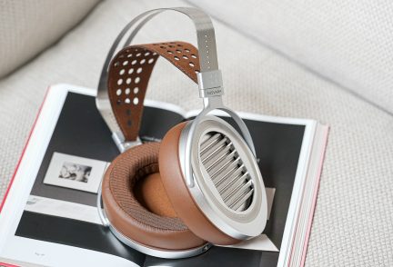 Un casque audio argenté avec coussinets marron repose sur un livre ouvert avec une couverture blanche et rouge