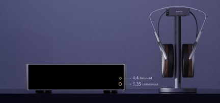 Eestvaates hallist metallist, musta esipaneeliga ristkülikukujuline kõrvaklapivõimendi, millel on kaks kuldset jack-pesa siltidega „4.4 Balanced” ja „6.35 UnBalanced”, paigutatud vasakule tumedast puidust korpustega, metallist peapaela ja sobiva vertikaalse alusega ümbritsetud üle-kõrva kõrvaklappidest, ühtlasel sinisel taustal.
