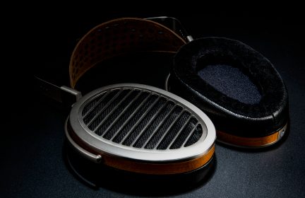 Un casque audio avec des oreillettes ovales, une grille métallique, un contour en bois et un arceau perforé en cuir