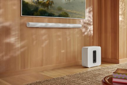 Vue d'angle d'une barre de son blanche fixée sur un mur en bois, caisson de basse blanc au sol, tapis tissé beige