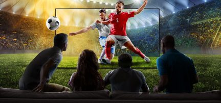 Large flat-screen black TV, glass surface, front view from behind four spectators, displaying a football match with an image effect extending beyond the screen