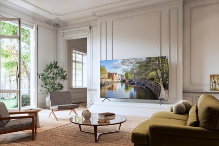 Large flat-screen black TV with a slim metal frame and glass surface, mounted on a thin central stand, front view in a bright living room with contemporary decor