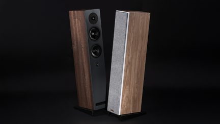 Deux enceintes colonnes en bois finition noyer, une avec façade noire et haut-parleurs visibles, l'autre avec grille en tissu gris