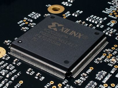 Processeur Xilinx XC2C64 sur circuit imprimé noir avec composants électroniques dorés, vue rapprochée de dessus