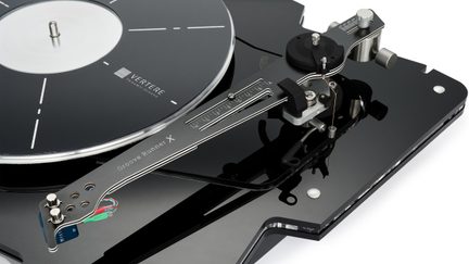 Platine vinyle noir brillant en acrylique vue de trois-quarts supérieur, plateau circulaire noir à repères blancs, bras de lecture gris métallisé portant l’inscription « Groove Runner X », repère gradué et câbles multicolores apparents