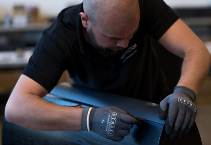 Vue rapprochée de trois-quarts d’un homme ganté de gris travaillant sur une surface courbe en bois noir à grain apparent