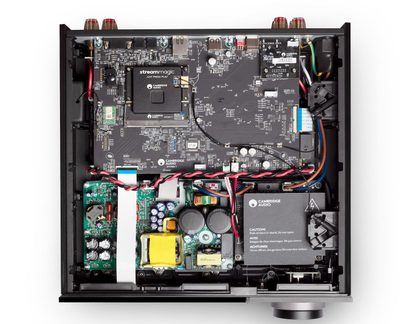Top view of the inside of a black metal hi-fi audio device case, with dense green and black printed circuit boards, a transformer wrapped in yellow tape, large black cylindrical capacitors, and twisted red and black cables