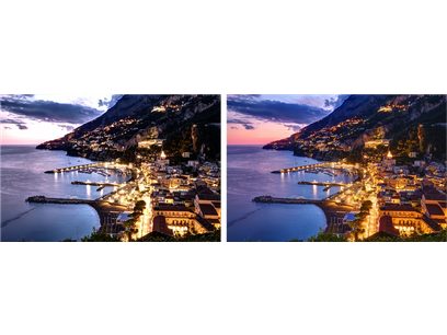 Vue aérienne nocturne d'une ville côtière illuminée, bâtiments denses au bord de l'eau, montagnes rocheuses en arrière-plan