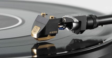 Testina di lettura per giradischi in vinile nera e dorata, vista ravvicinata di profilo, appoggiata su un disco in vinile nero