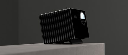 Boîtier électronique rectangulaire noir en métal doté de nombreuses ailettes verticales argentées et d’une ouverture circulaire brillante sur la façade, posé sur un petit support incliné, vue en perspective trois-quarts avant