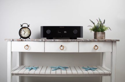 Table console blanche avec 3 tiroirs, horloge noire, amplificateur noir, plante verte en pot, 3 étoiles de mer bleues
