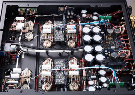 Top view of the inside of an audio amplifier, black metal casing, row of large black cylindrical capacitors, green and black printed circuit boards, multiple pinkish-beige resistors, and red, blue, white, and black cables