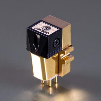 Cellule phono vue en trois-quarts, corps métallique doré lisse avec façade plastique noire et insert bois clair gravé, stylet saillant à l’avant et quatre broches dorées sous la base