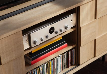 Amplificator audio integrat din lemn cu față argintie, butoane rotative negre și bandă roșie, pe raft cu CD-uri