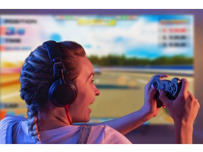 Jeune femme de profil portant un casque audio bleu et rouge, tenant une manette de jeu noire dans ses mains, regard concentré