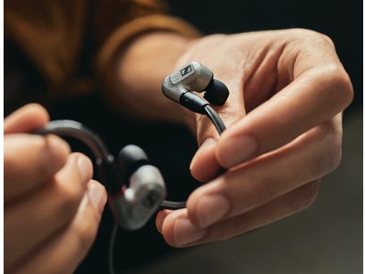 Mains tenant un casque intra-auriculaire Sennheiser IE 600 noir, gros plan sur les écouteurs métalliques