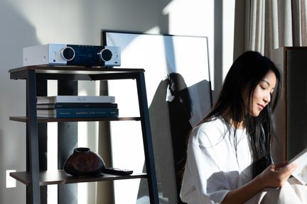 srebrny amplituner stereo Onkyo na designerskiej półce z drewna i metalu w jasnym salonie z czytającą kobietą