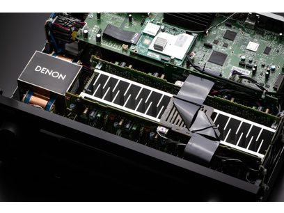 Indvendigt syn af en sort Denon AVC-X3800H-forstærker, der viser printkortet med komponenter, kølevinger og blæsere