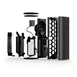 Vue éclatée latérale d’une enceinte cylindrique noire en plastique et métal, grille avant perforée, structure interne alvéolaire, haut-parleur, carte électronique, batterie et capuchons circulaires
