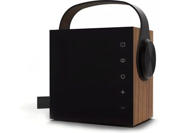 Enceinte bluetooth portable Morel Biggie chêne, vue de trois-quarts avant droit, boîtier cubique mêlant flancs en placage de chêne et façade noire mate, munie d’une poignée arquée noire supérieure, d’une large molette circulaire noire latérale droite et d’icônes de commandes tactiles alignées verticalement