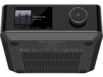Ampli hi-fi intégré stéréo WiiM Amp Ultra noir à boîtier métallique, vue en contre-plongée montrant l’écran couleur supérieur, le large bouton rotatif rétroéclairé et le dessous muni de patins et de fentes de ventilation