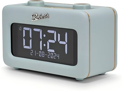 Radio-rēveil Roberts Revival Rest gaisā zilā mākslīgās ādas izstrādājumā, trīs ceturtdaļu priekšskats, ar lielu melnu digitālo ekrānu ar baltiem cipariem, smalkām zelta apmaliem un divām apaļām riteņveida vadības ratiņām uz augšpuses
