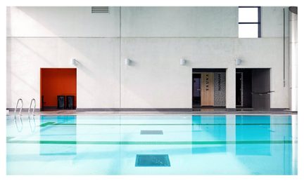 Piscine intérieure rectangulaire avec eau turquoise, sauna rouge et portes grises dans un bâtiment moderne en béton