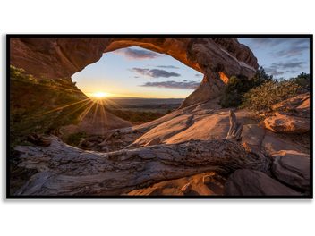 Arche naturelle rocheuse au coucher du soleil, vue à travers depuis l'intérieur, avec rayons de soleil et ciel nuageux coloré